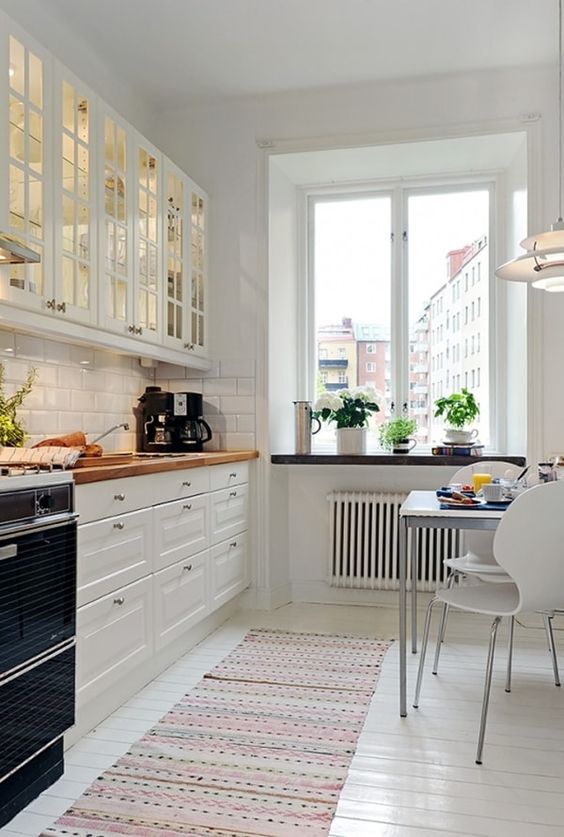 a lovely white Nordic kitchen with butcherblock countertops and modern chairs plus a large window with much natural light