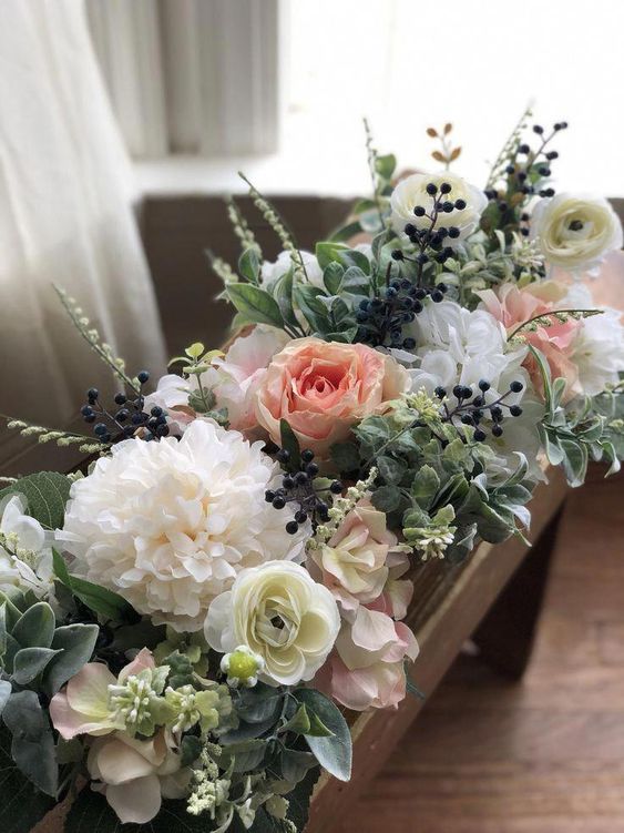 a lush faux floral arrangement of white, pastel blooms, greenery and berries in a wooden box