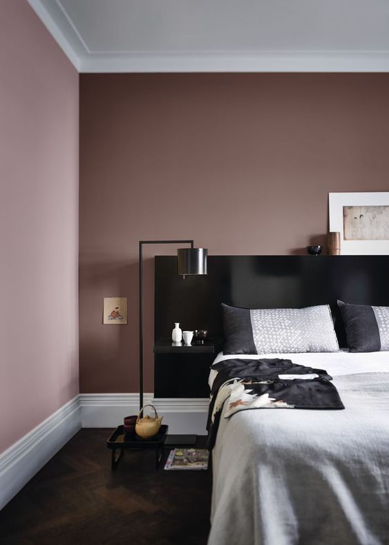 a mauve bedroom with a black bed, grey and black bedding, black floor lamps and pretty artworks