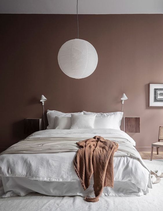 a mauve bedroom with a cozy white bed, mauve nightstands, a paper lamp and a rust blanket