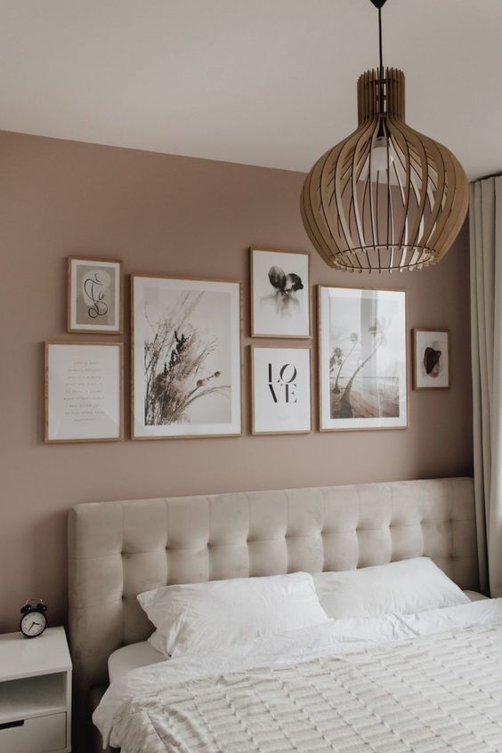 a mauve bedroom with a creamy upholstered bed, a nightstand, a lovely gallery wall and a plywood pendant lamp
