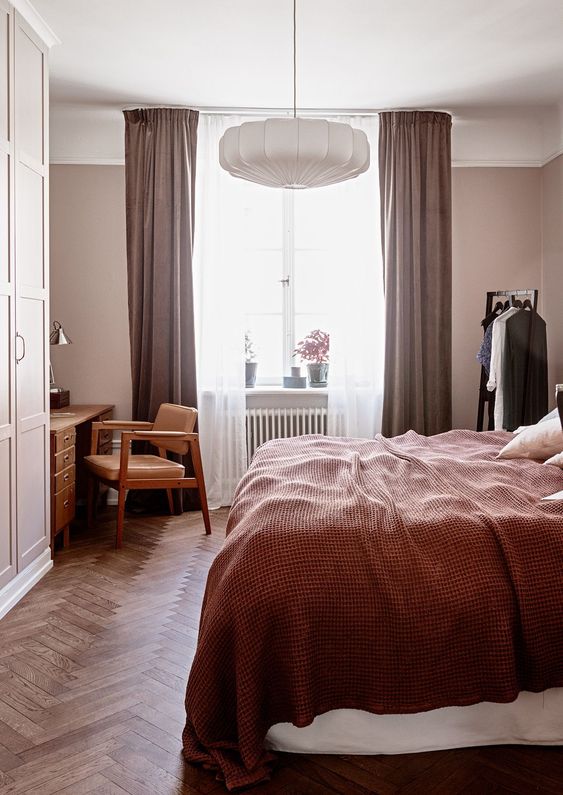 A mauve bedroom with mid century modern furniture, mauve curtains, burgundy bedding and a paper lamp