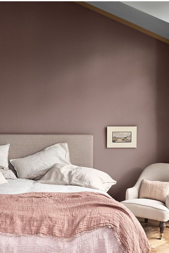 a mauve bedroom with neutral furniture, a pink blanket and neutral bedding and bold artworks