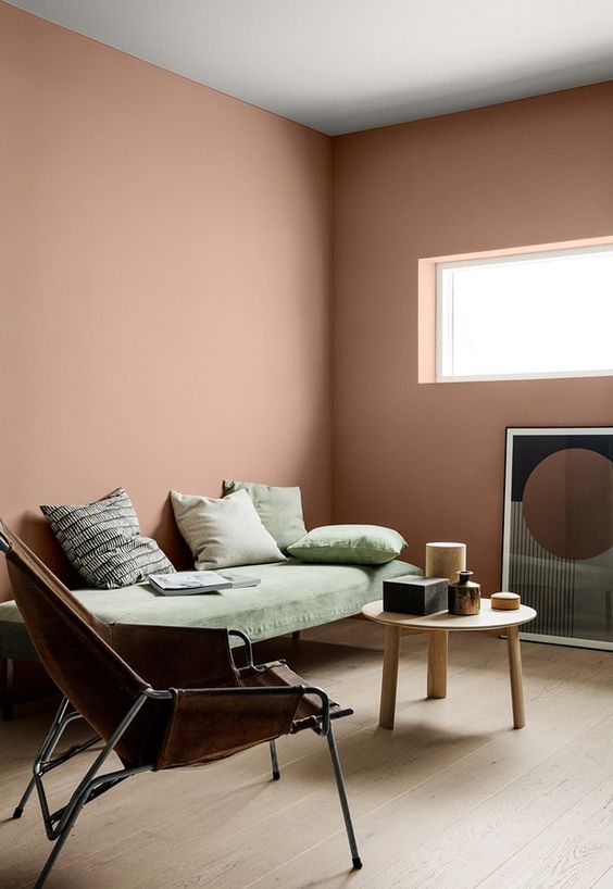 a mauve living room with a green daybed, a leather chair, a round wooden table and a catchy artwork