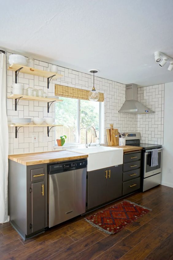 a mid-century modern grey kitchen with open shelves, a white tile backsplash and butcherblock countertops is a chic space