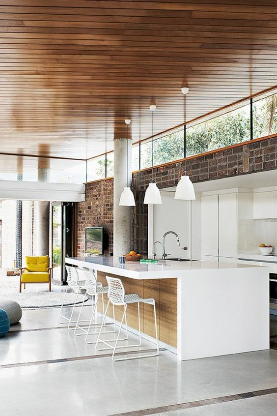 A mid century modern kitchen with a brick wall, white minimalist cabinetry and clerestory windows that bring in light