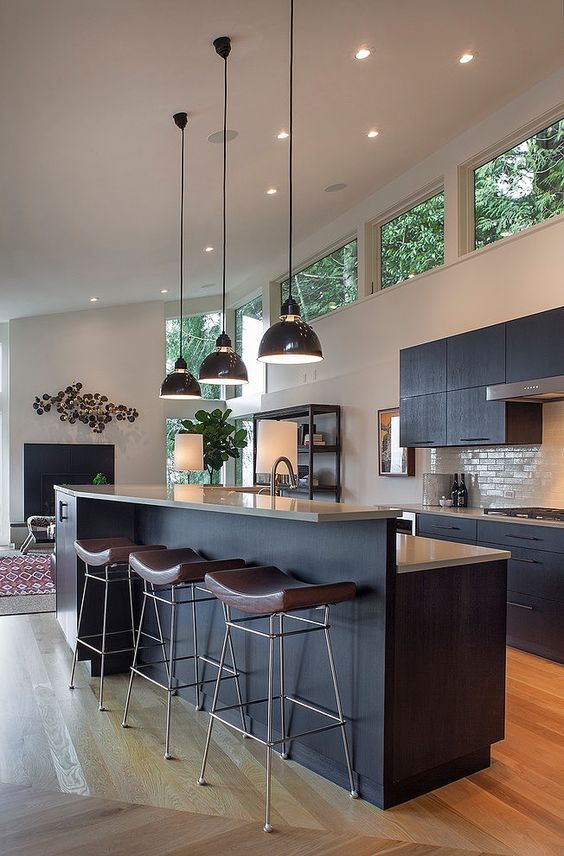 A mid century modern kitchen with black cabinetry, clerestory windows for more light, pendant lamps and leather chairs