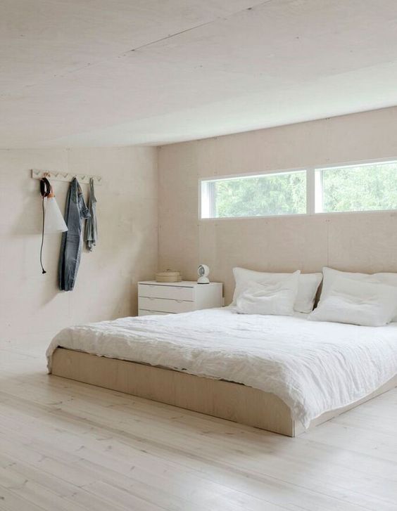 a minimalist bedroom in light shades, with a dresser and a bed plus clerestory windows for more light