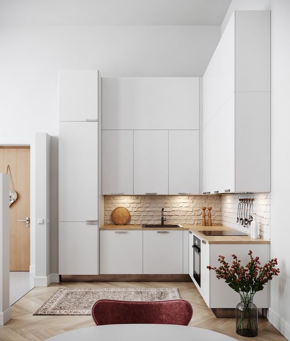 a minimalist white L-shaped kitchen with a brick backsplash, butcherblock countertops and built-in lights