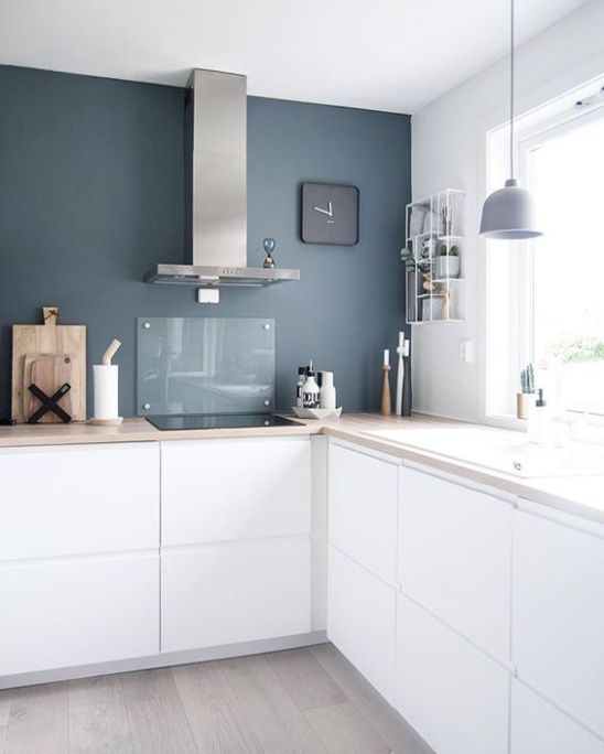 A minimalist white L shaped kitchen with butcherblock countertops, a glass backsplash and a pendant lamp