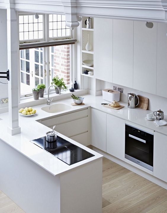 A minimalist white U shaped kitchen with matching countertops and a backsplash, with built in appliances