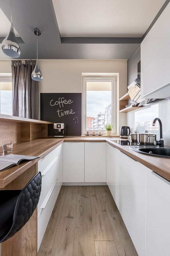 a minimalist white kitchen with butcherblock countertops, a white glass backsplash and a chalkboard plus an office space