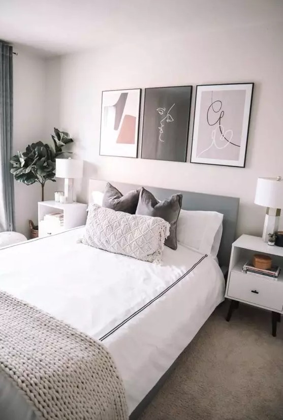 a modern and welcoming bedroom with a grey bed and neutral bedding, white nightstands, a small gallery wall and a potted plant