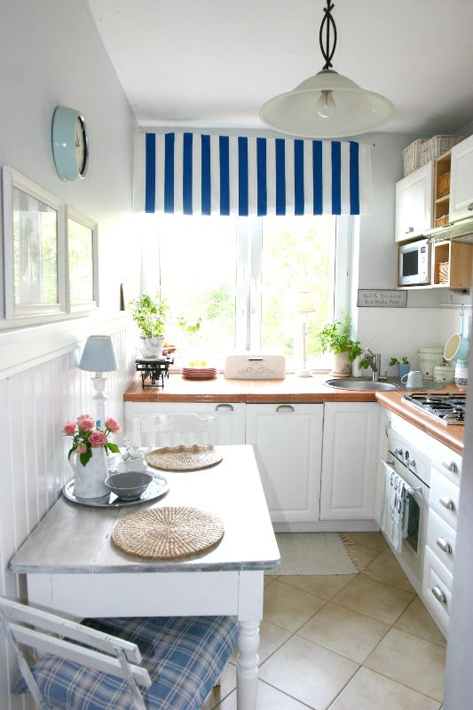 A modern coastal L shaped kitchen with rich stained butcherblock countertops, printed blue textiles and potted greenery