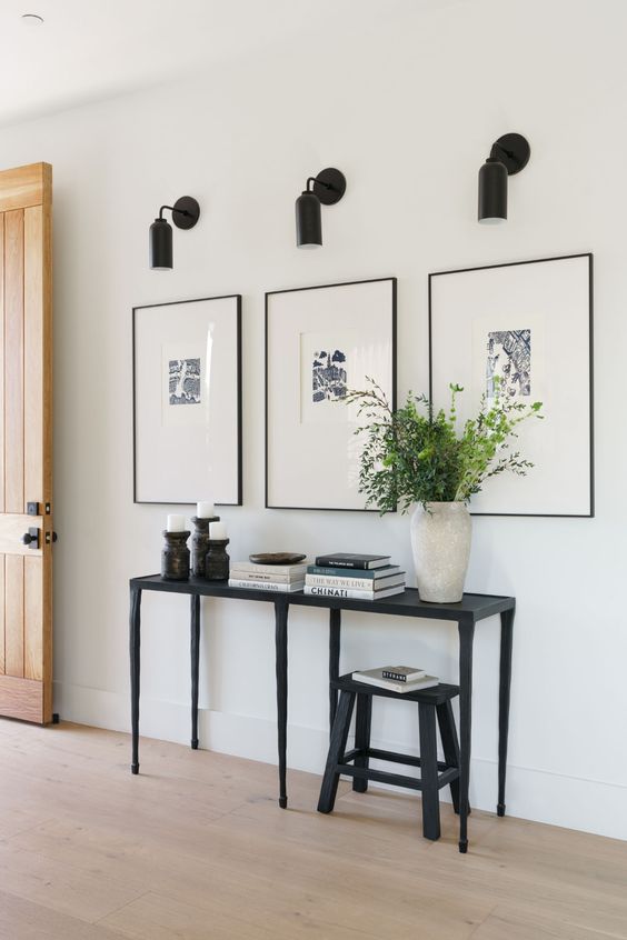 a modern farmhouse entryway with a grid gallery wall, a black console table and a stool, candles and sconces
