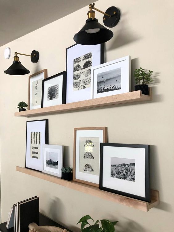 a modern farmhouse gallery wall with light stained wooden ledges, black and white artworks, potted greenery and elegant black sconces