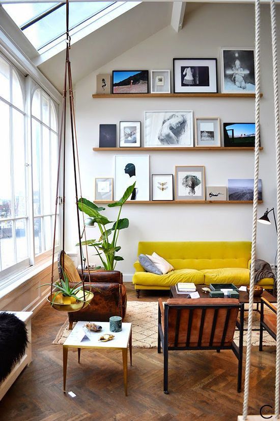 a modern space with a gallery wall on stained wooden ledges, with black and white and colorful artworks that is located rather high