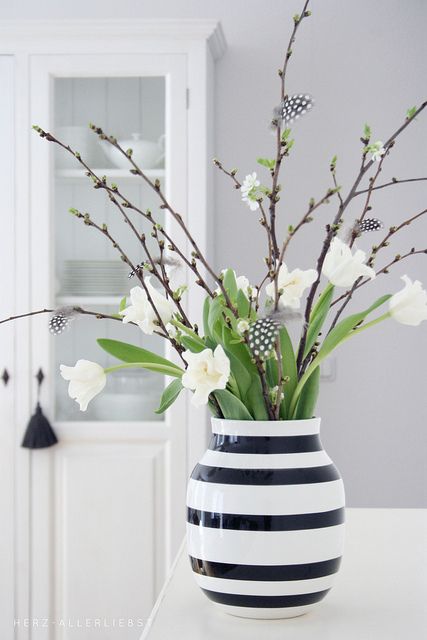 a monochromatic Easter centerpiece of a striped vase, whiet tulips, willow and feathers attached