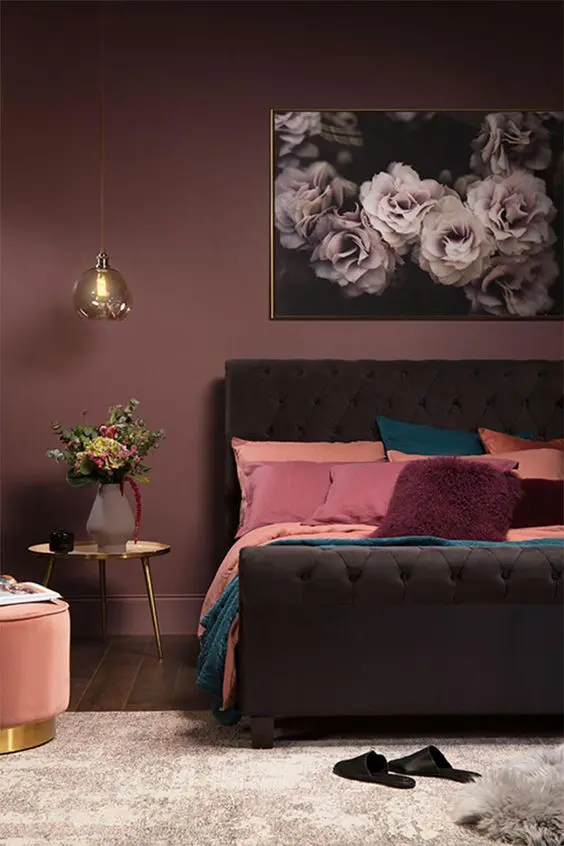 a moody mauve bedroom with a dark brown upholstered bed, pink, peachy and teal bedding, touches of gold and a floral artwork