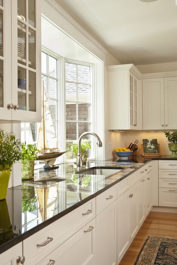 a neutral farmhouse kitchen with black countertops and a pretty bow window that fills the space with natural light
