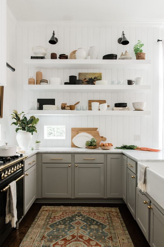A pretty U shaped kitchen with grey shaker style cabinets, white countertops, white floating shelves and brass and gold touches for elegance