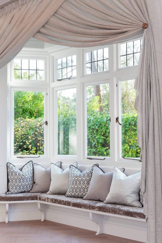 a refined bow window nook with a windowsill seating space with pillows and exquisite neutral curtains