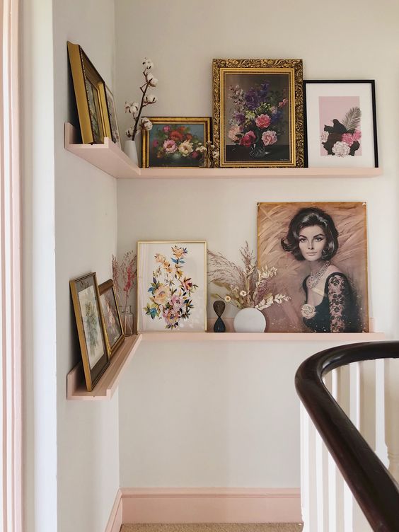 a refined gallery wall done with blush corner ledges, vintage artworks in gold and black frames, dried leaves and blooms in vases