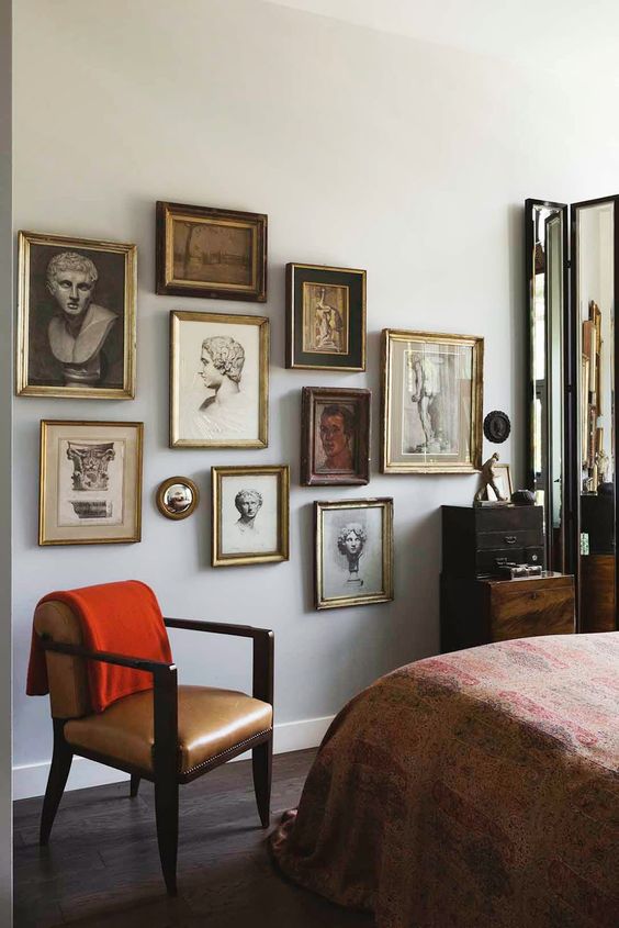 a refined gallery wall with gilded frames and vintage portraits and statue heads is a chic idea for a vintage space