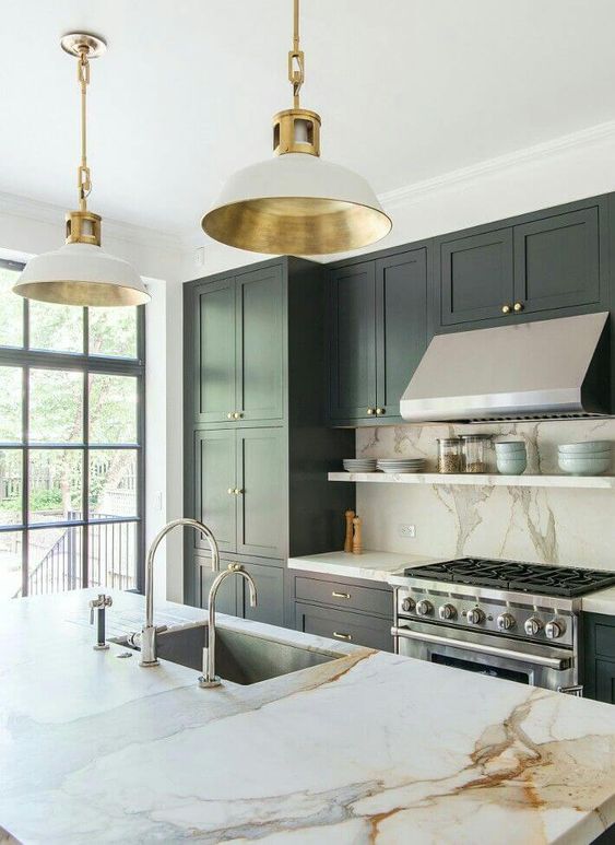 a refined hunter green kitchen with white marble countertops and a backsplash, elegant white and gold lamps and stainless steel appliances