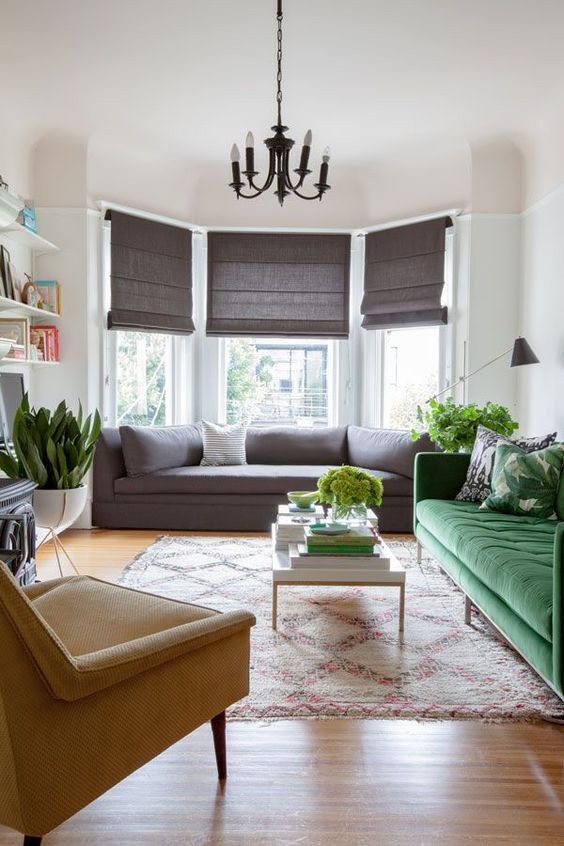 A refined modern living room with a bow window and a sofa built in there, a green sofa, a mustard chair and potted plants