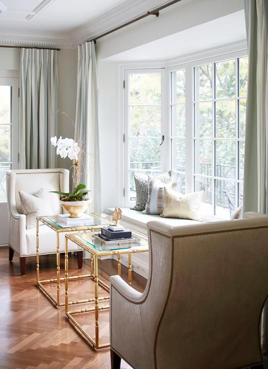 a refined space with a bow window and a daybed on the windowsill, refined chairs and glass and metal tables