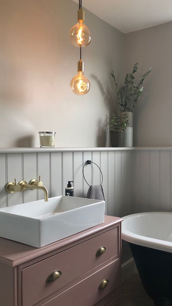 A refined vintage inspired bathroom with a mauve vanity, black and white appliances and hanging bulbs