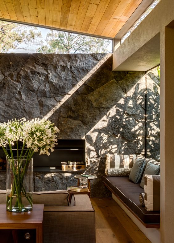 a rustic living room with a stone accent wall, chic furniture, a large window and some clerestory ones for more light