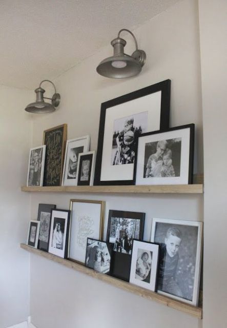 a rustic vintage gallery wall with light stained wooden ledges, family pics in mismatching frames and vintage wall sconces over them
