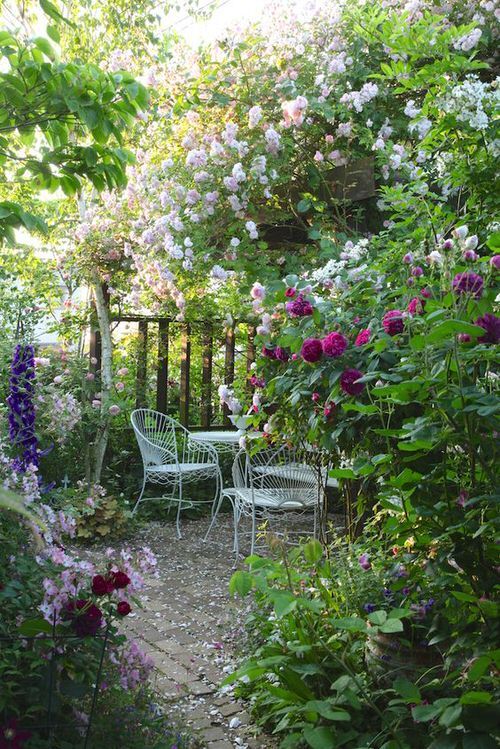 a small and chic garden dining space under blooming bushes, with refined forged garden furniture is cool