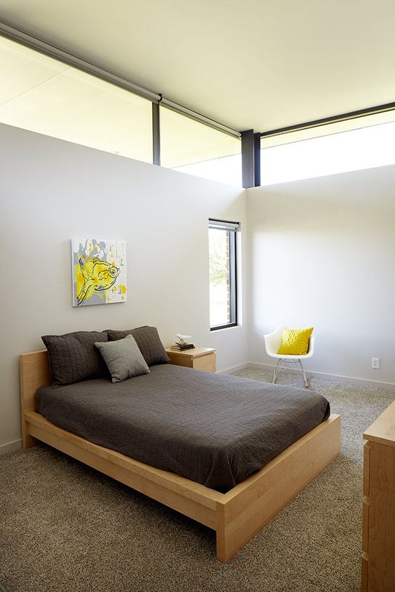 a small contemporary guest bedroom with neutral walls, blonde wood furniture, bright yellow touches and clerestory windows for more ligth here