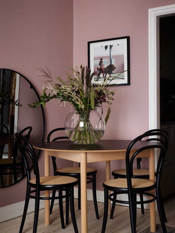 a small dining space with mauve walls, a chic table and elegant vintage chairs plus a large round mirror