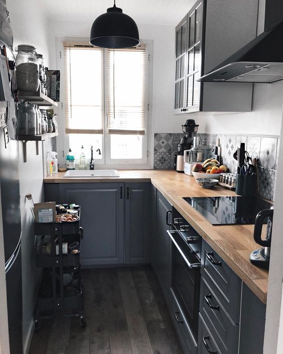 A small graphite grey L shaped kitchen with a catchy printed backsplash and butcherblock countertops is a cool space