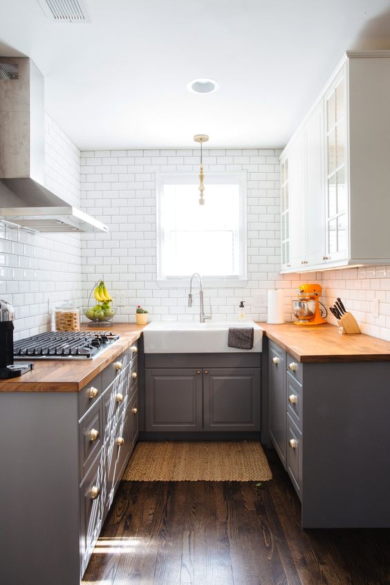 a small grey farmhouse kitchen with butcherblock countertops and white tiles on the walls is chic