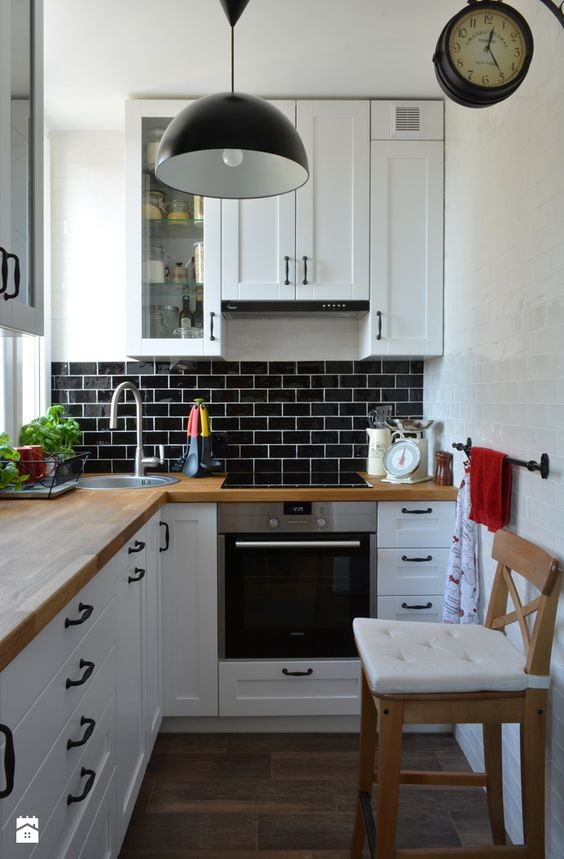 a small white L-shaped kitchen with butcherblock countertops and a black tile backsplash plus a black pendant lamp