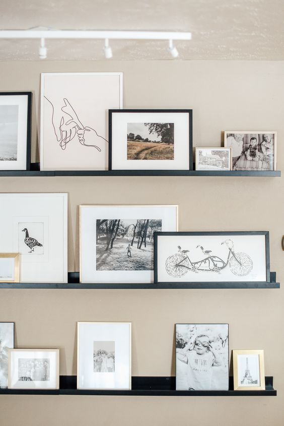 a stylish contemporary gallery wall with black ledges, black and white artworks in blonde wood, white and black frames