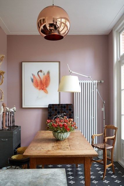 a stylish dining room with mauve walls, a copper lamp, a wooden table and vintage chairs, a dark chest, a bold artwork