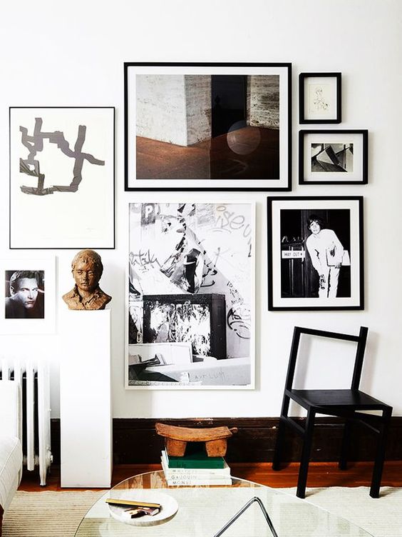 a stylish free form gallery wall with black and white frames and built around a central painting is a chic idea