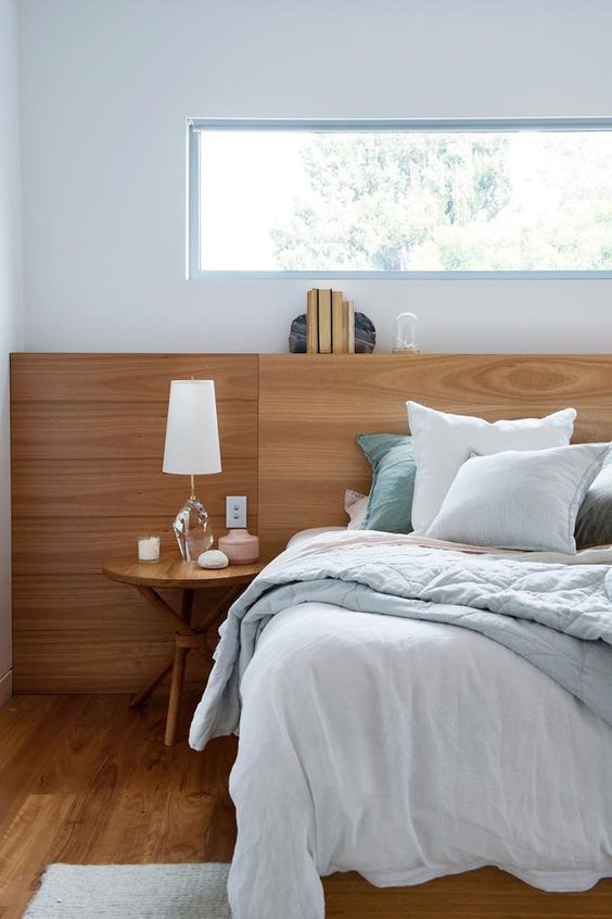 a stylish modern bedroom with much wood, a comfy bed with blue bedding, a round table and a clerestory window for privacy