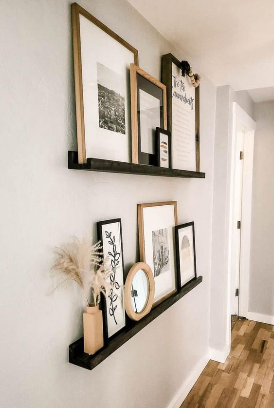 a super chic gallery wall with black ledges, black and white artworks in black and stained frames, pampas grass and wooden beads