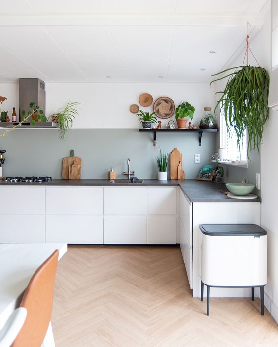A white L shaped boho kitchen with a grey backsplash, grey stone countertops, potted greenery is lively and cool