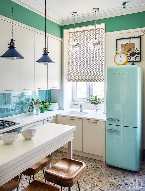 A white L shaped kitchen with a blue fridge, pendant lamps and patterned tiles on the floor is a pretty and catchy space