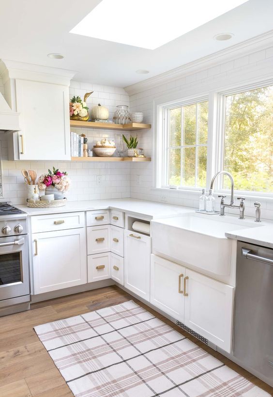 a white L-shaped kitchen with brass handles, open shelves and windows plus a skylight is a very welcoming space