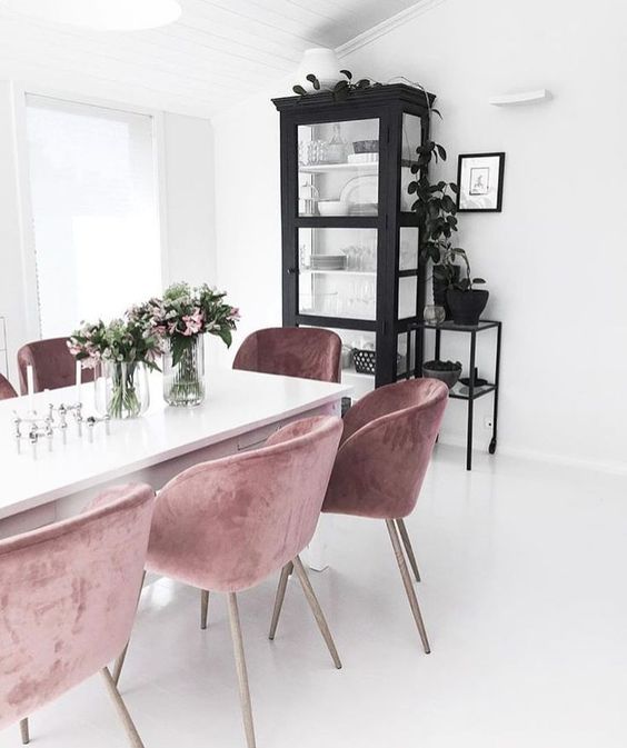 a white Nordic dining room with a black buffet and mauve chairs, some plants and blooms