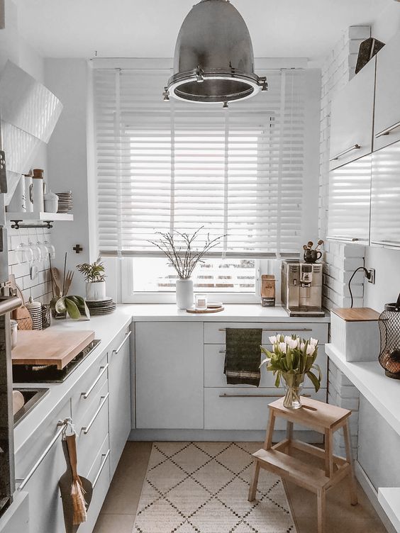 A white Scandinavian L shaped kitchen with a white tile backsplash and countertops, wooden surfaces is super cool